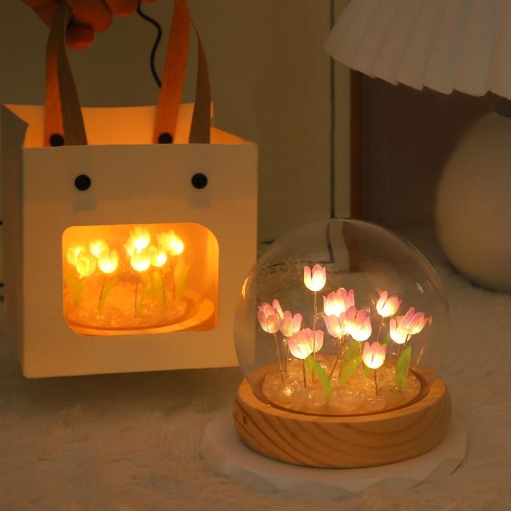 Decorative light bulb with tulip design inside a glass dome on a wooden base, next to a small bag with lights.